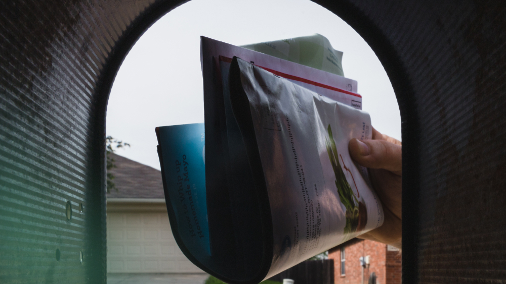 Hand reaching into mailbox to retrieve a stack of mail and flyers.