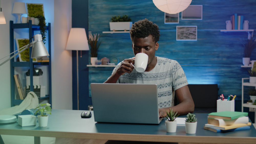Freelancer sipping coffee while working remotely on a laptop.