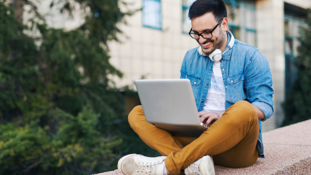Freelancer working remotely on a laptop outdoors with a happy expression.